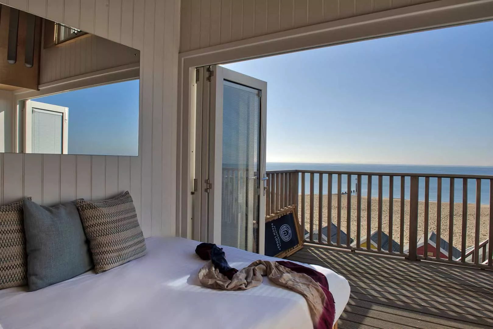 Neatly made bed with bi-fold doors wide open to see the sea