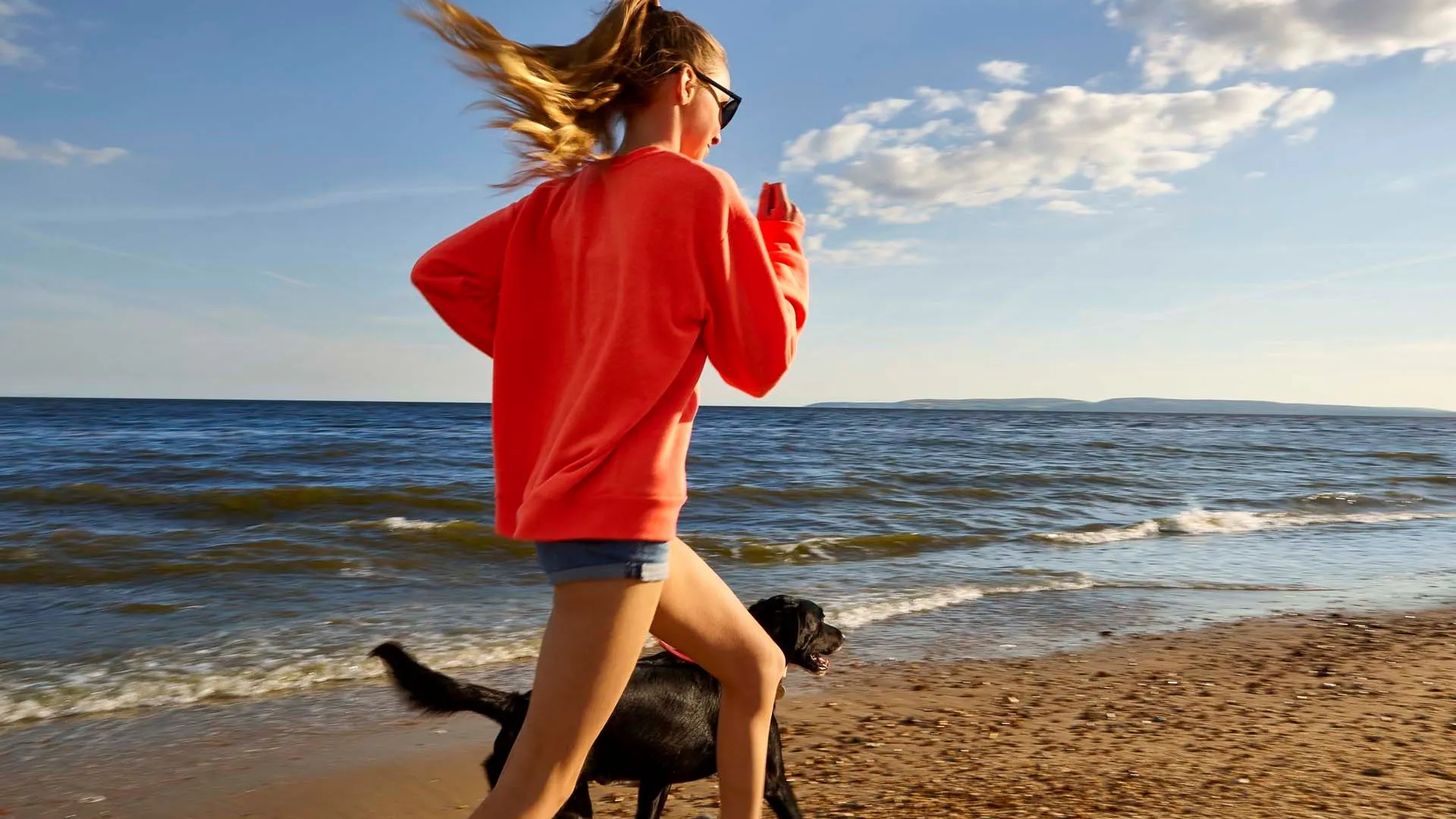 Girl going for a beach run with black dog