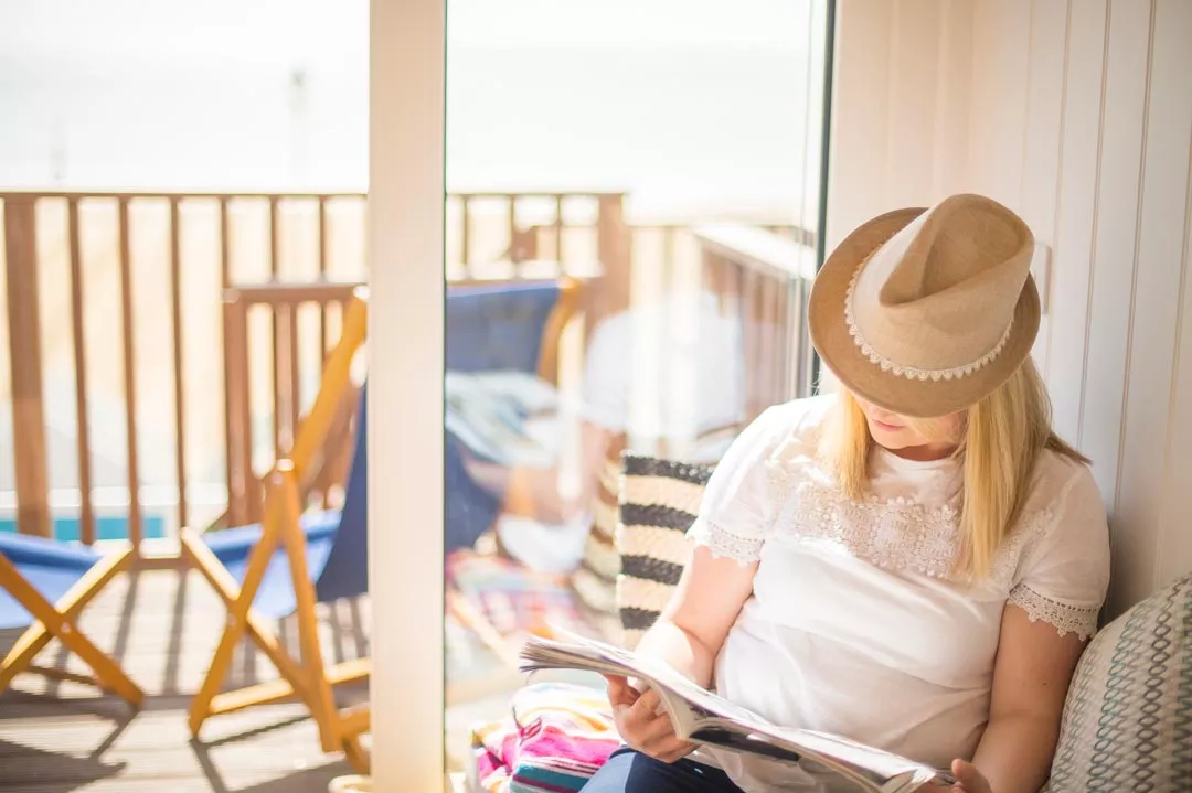 A person with a hat on sitting in a lodge reading a newspaper