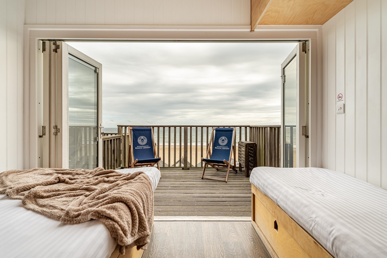 Two beds inside the beach lodge looking out of the patio doors towards the balcony with deckchairs.