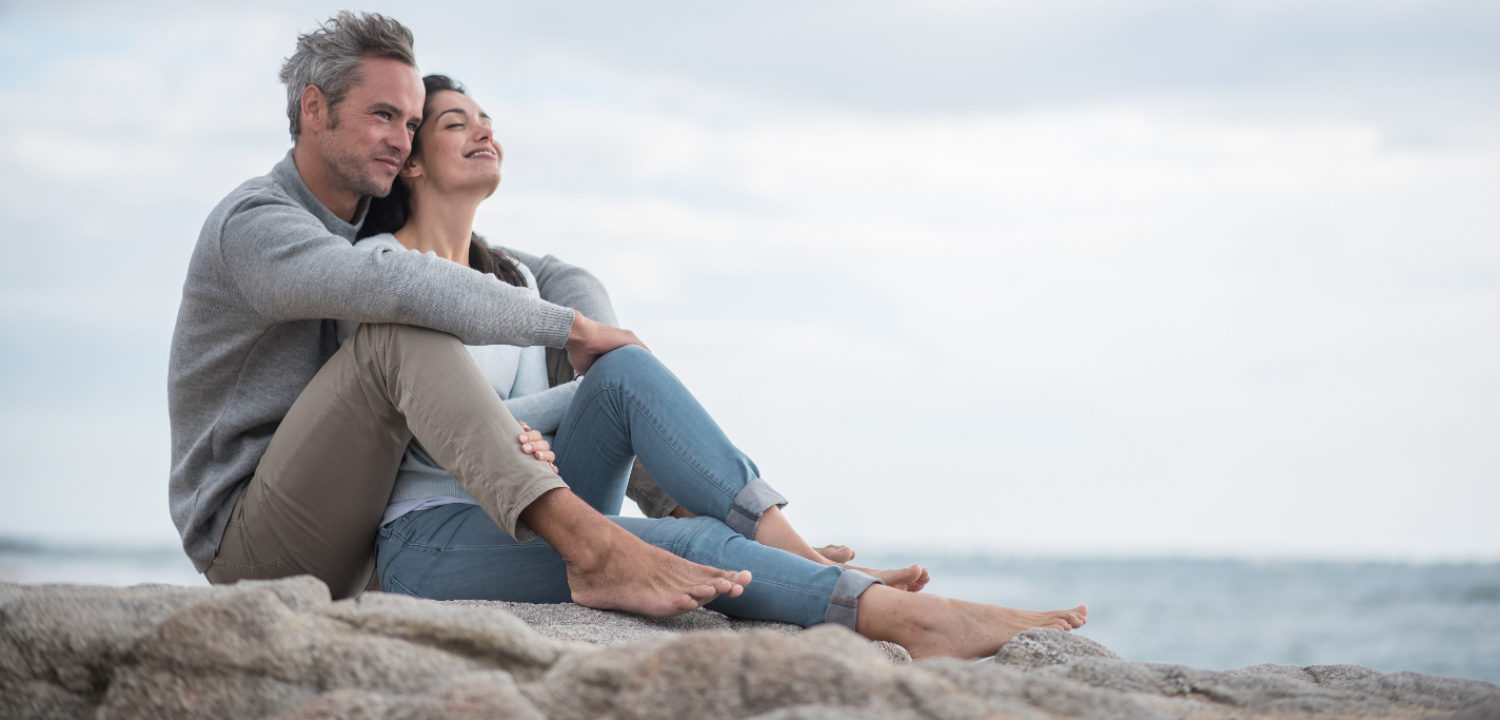 A couple sitting on rocks, looking out at the sea