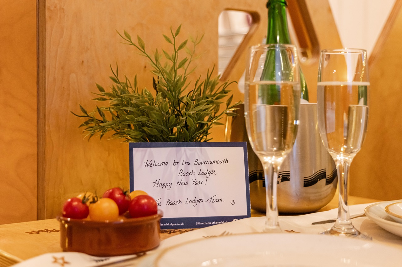 A handwritten message from the Lodge team wishing guests a happy new year, next to two glasses of wine.