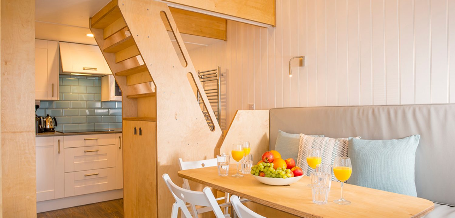 Interior of a beach lodge showing the dining area and kitchen with stairs up to the top floor