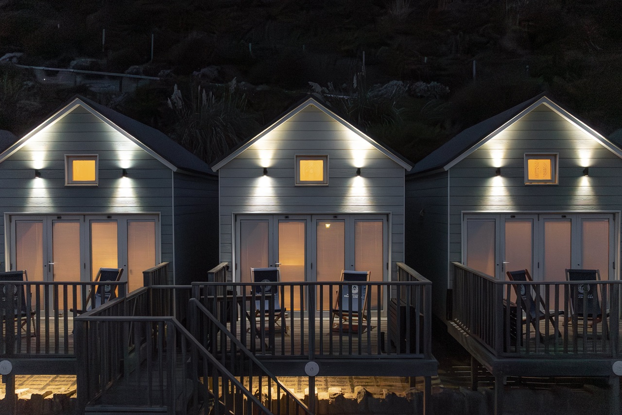 A view of the front of three lodges at night, with interior and exterior lighting on.