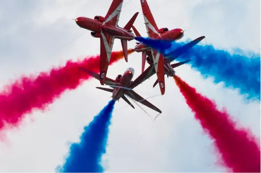 Red arrows doing a tight maneuver with red and blue smoke at the air show