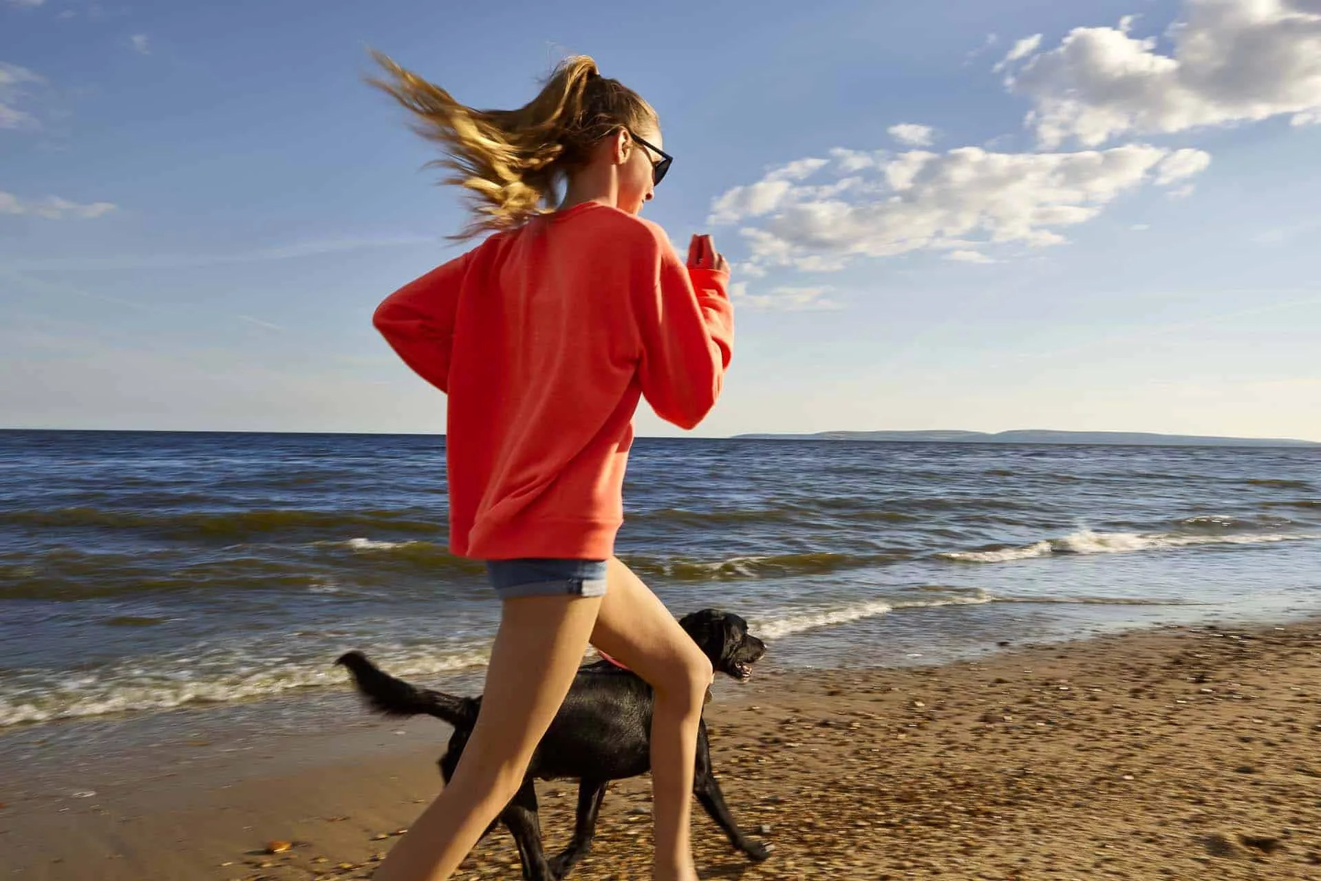 Young girl running along Bournemouth beach with her Black Labrador